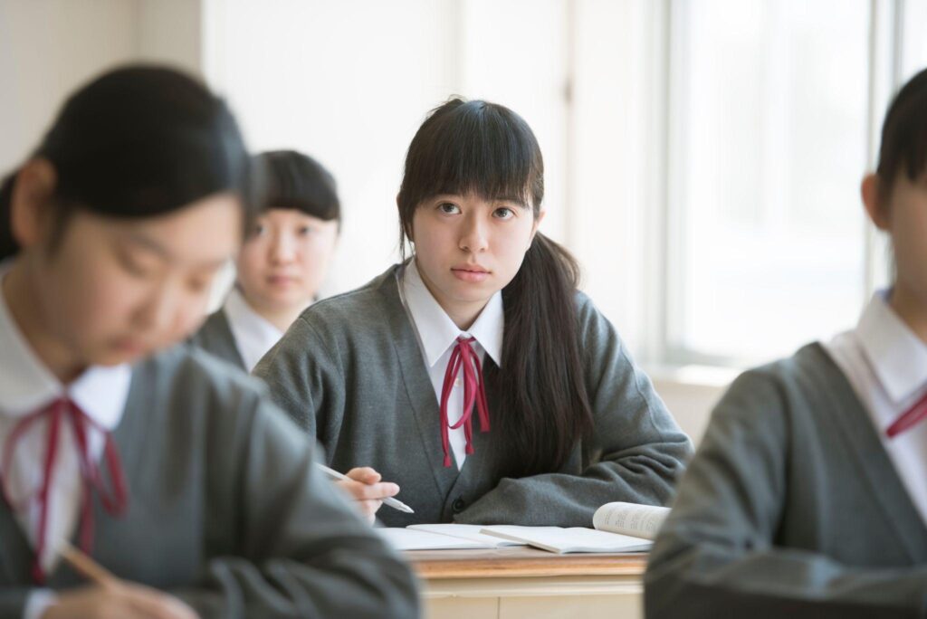 教室で授業を受けている女子高校生が前方をまっすぐ見つめている様子。