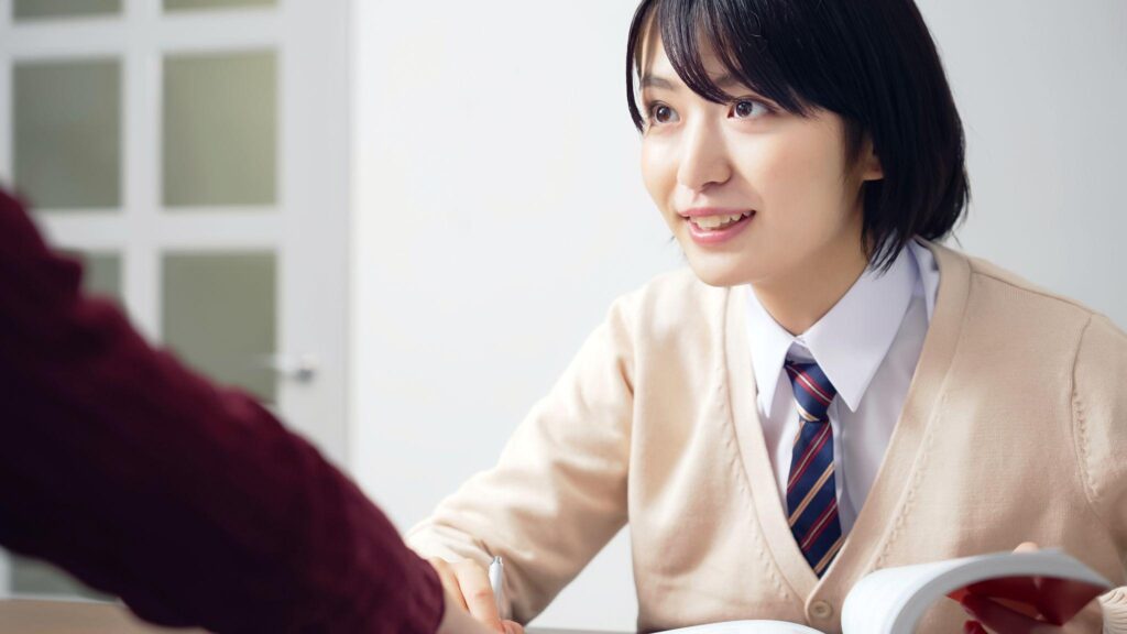 机で本を開きながら相手と会話している若い女性